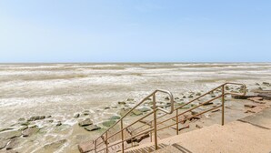 A coastal walkway with steps leading down to the shore, surrounded by rocks and seaweed. - 3 Pools and 2 Hot Tubs, Walk to the Beach (Galveston)