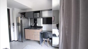 Una camera d'albergo compatta con angolo cottura, un letto e una piccola scrivania.