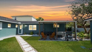 A backyard with a covered patio, two rocking chairs, a grill, and a stone pathway leading to the house. - Coastal Blue Escape (St. Augustine)
