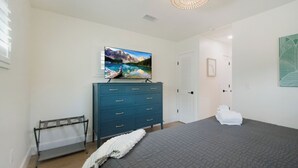 A bedroom with a bed, a dresser, a television on top of the dresser, and a door in the background. - Coastal Blue Escape (St. Augustine)