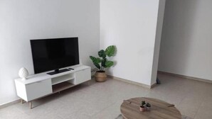 A modern living room with a flat-screen TV on a white TV stand, a round wooden coffee table, and a potted plant. - E&S Apartment (Syracuse)