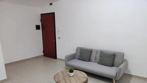A minimalist living room with a grey sofa, a round coffee table, and a red door. - E&S Apartment (Syracuse)