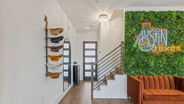 Un couloir moderne avec un escalier en bois, un panneau néon indiquant « Austin, Texas », et un mur végétal fixé au mur.