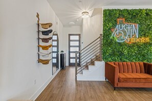 A modern hallway with a wooden staircase, a neon sign reading "Austin Texas", and a wall-mounted plant wall.