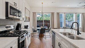 Une cuisine moderne avec des meubles blancs, des appareils en acier inoxydable et un coin repas comprenant une table et des chaises en verre.