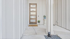 Un couloir avec une porte en bois, un paillasson et des plantes en pot.