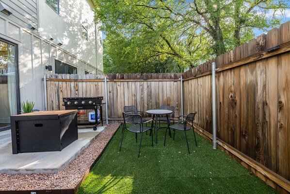 A backyard with a barbecue grill, a table, and chairs.