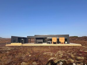 A modern, two-story building with large glass windows and a flat roof, situated in a natural landscape. - A peaceful, private luxury retreat w/hot tub in the heart of the Golden Circle (Grímsnes- og Grafningshreppur)