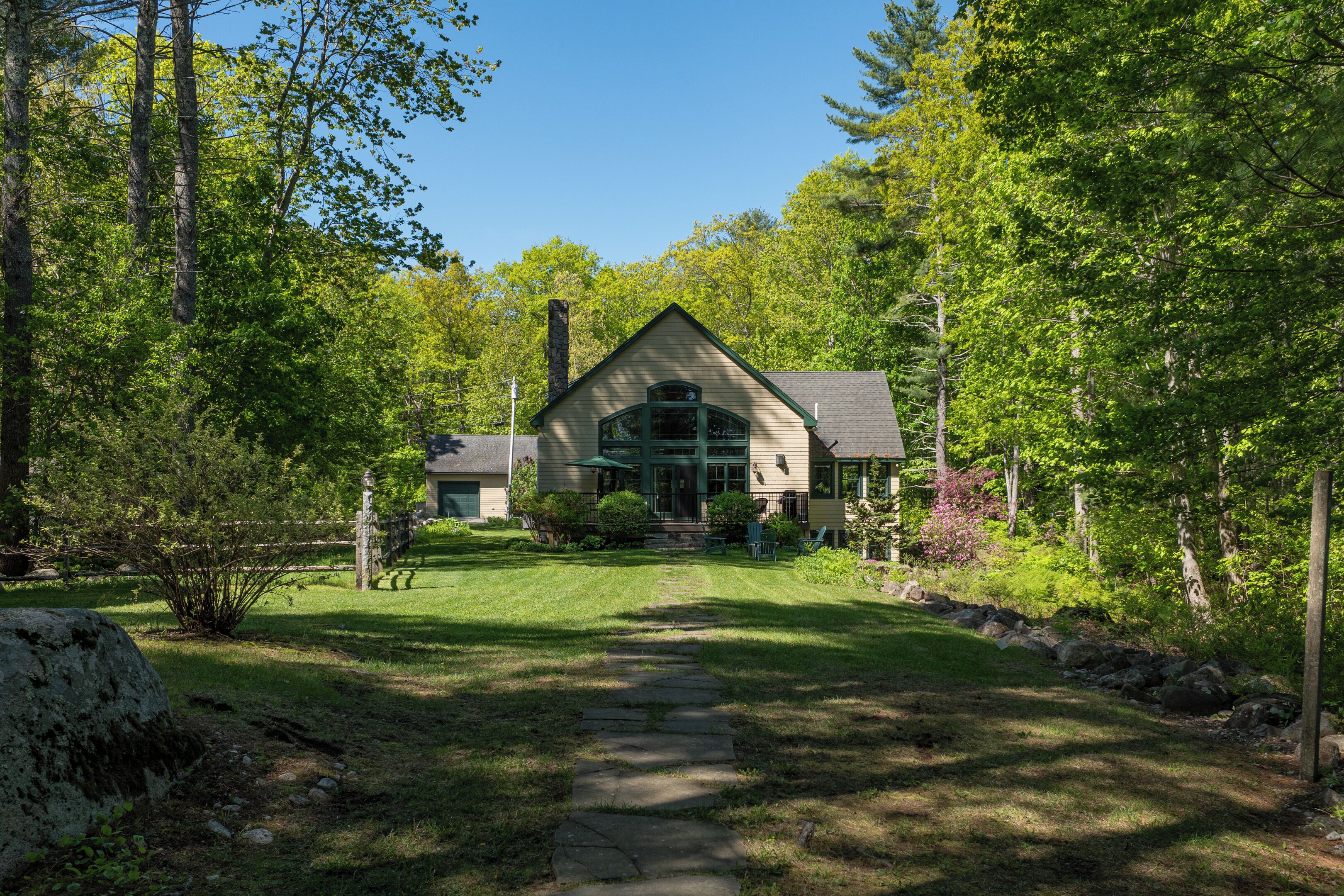 A house with a stone pathway leading to the front door, surrounded by lush greenery and trees.