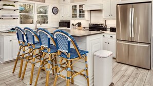Une cuisine moderne avec des meubles blancs, un réfrigérateur en acier inoxydable et un îlot central doté de tabourets de bar.