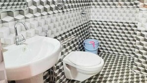 Un baño con piso y paredes de estampado geométrico, un lavamanos pedestal, un inodoro y una ducha.