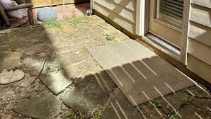 A house with a wooden deck, a stone patio, and a sliding glass door.