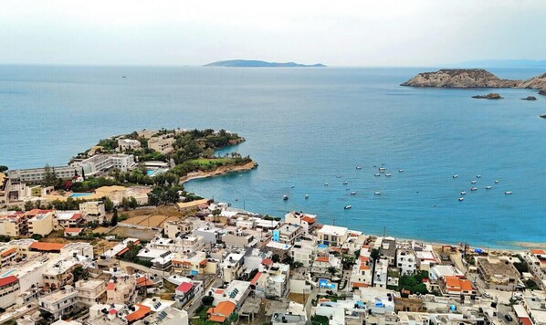 Une ville côtière avec des bâtiments le long du littoral, une petite île et des bateaux sur l’eau.