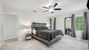 A bedroom with a bed, a nightstand, a ceiling fan, a window with curtains, and a mirror. - 4 bedroom home in Bridge City (Bridge City)
