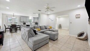 A modern living room with a grey sectional sofa, a dining area with a table and chairs, a kitchen with white cabinets, and a ceiling fan. - 4 bedroom home in Bridge City (Bridge City)