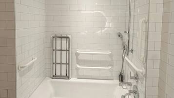 Un baño moderno con paredes de azulejos blancos, una bañera independiente y un área de ducha con mampara de vidrio.