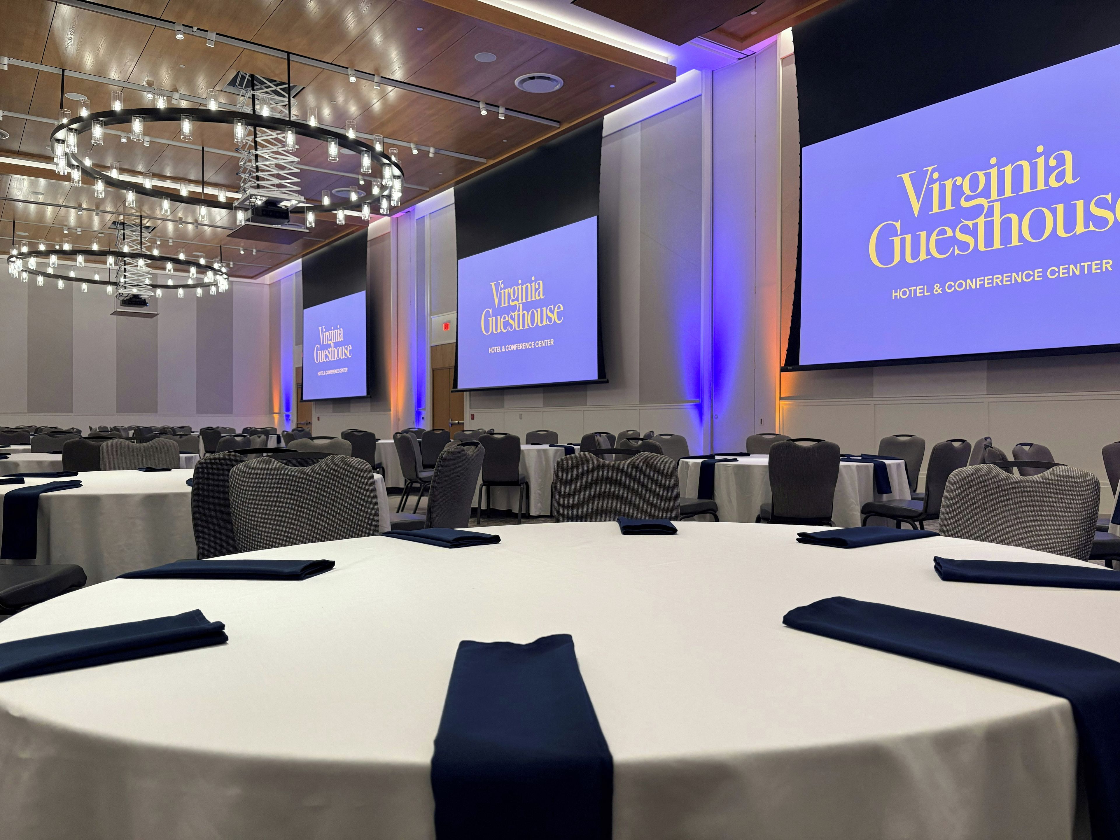 A conference room with round tables, chairs, and a large screen displaying 'Virginia Guesthouse' branding.