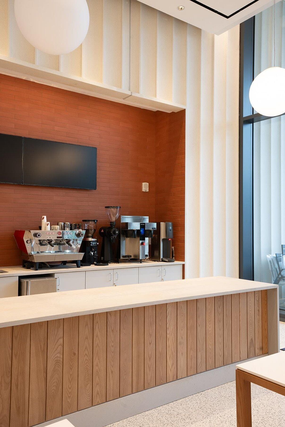 A modern bar area with a wooden counter, espresso machines, and a large window providing a view.