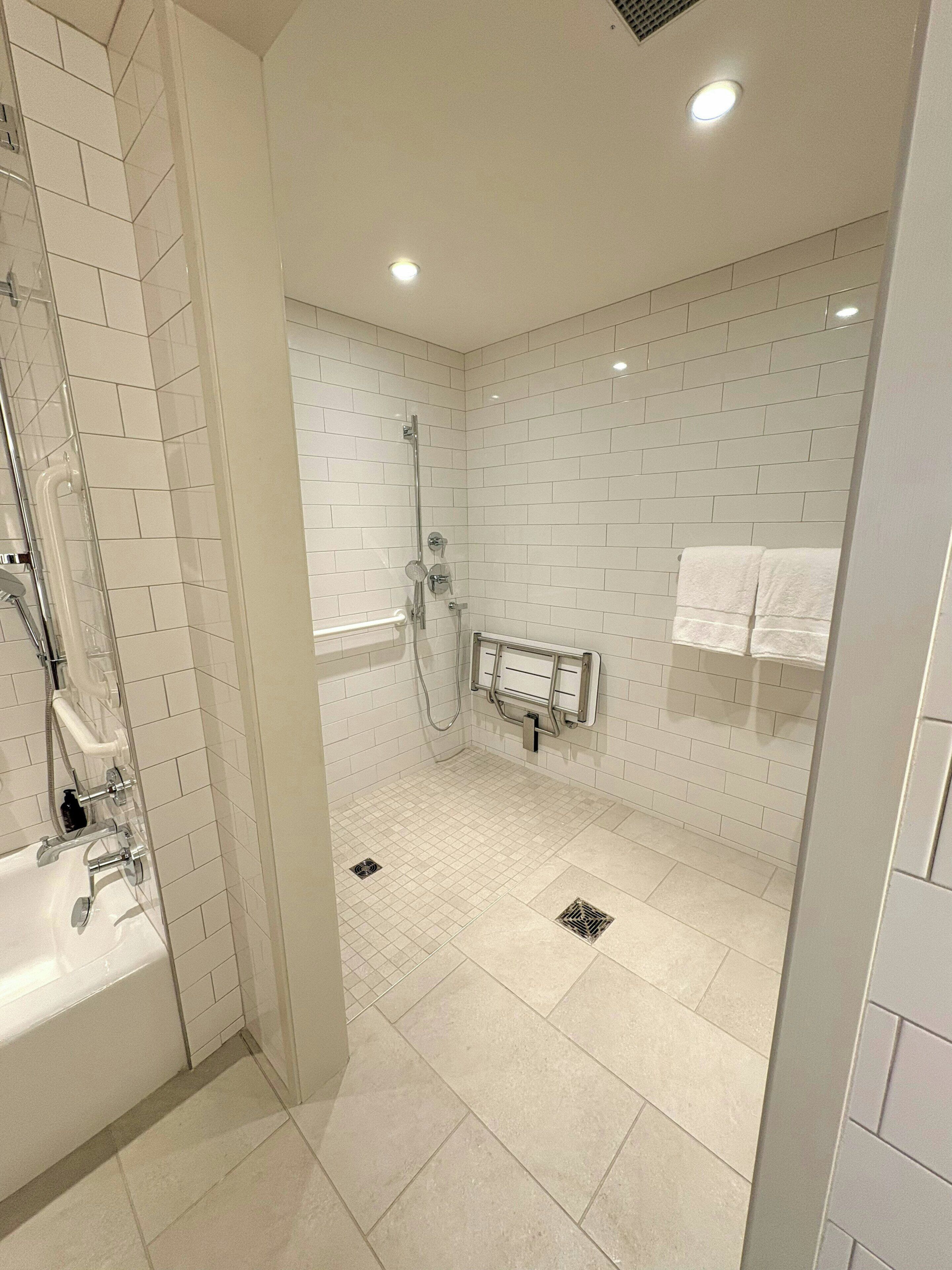 A modern bathroom with a glass-enclosed shower, white tiled walls, and a visible towel rack.