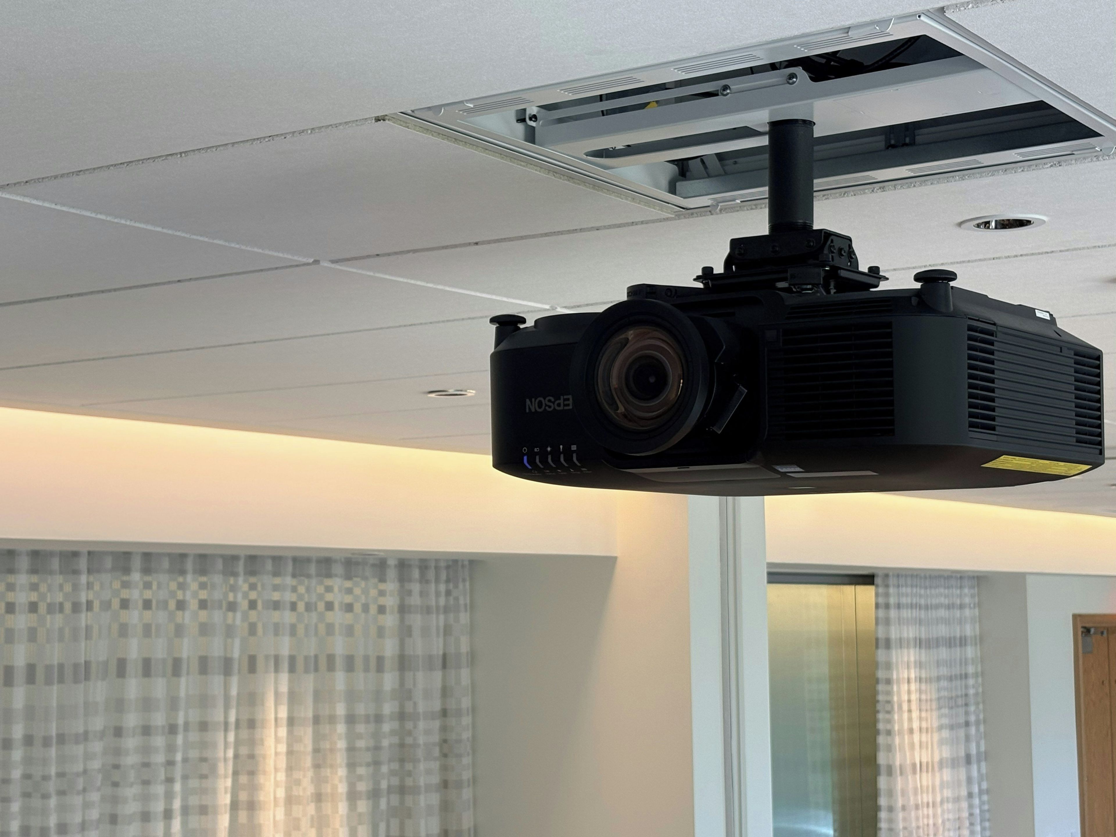Un projecteur fixé au plafond, dans une pièce dotée d’une fenêtre et de rideaux.