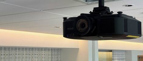 Un projecteur fixé au plafond, dans une pièce dotée d’une fenêtre et de rideaux.