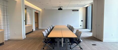 Una sala de conferencias con una larga mesa, sillas, piso alfombrado e iluminación empotrada en el techo.