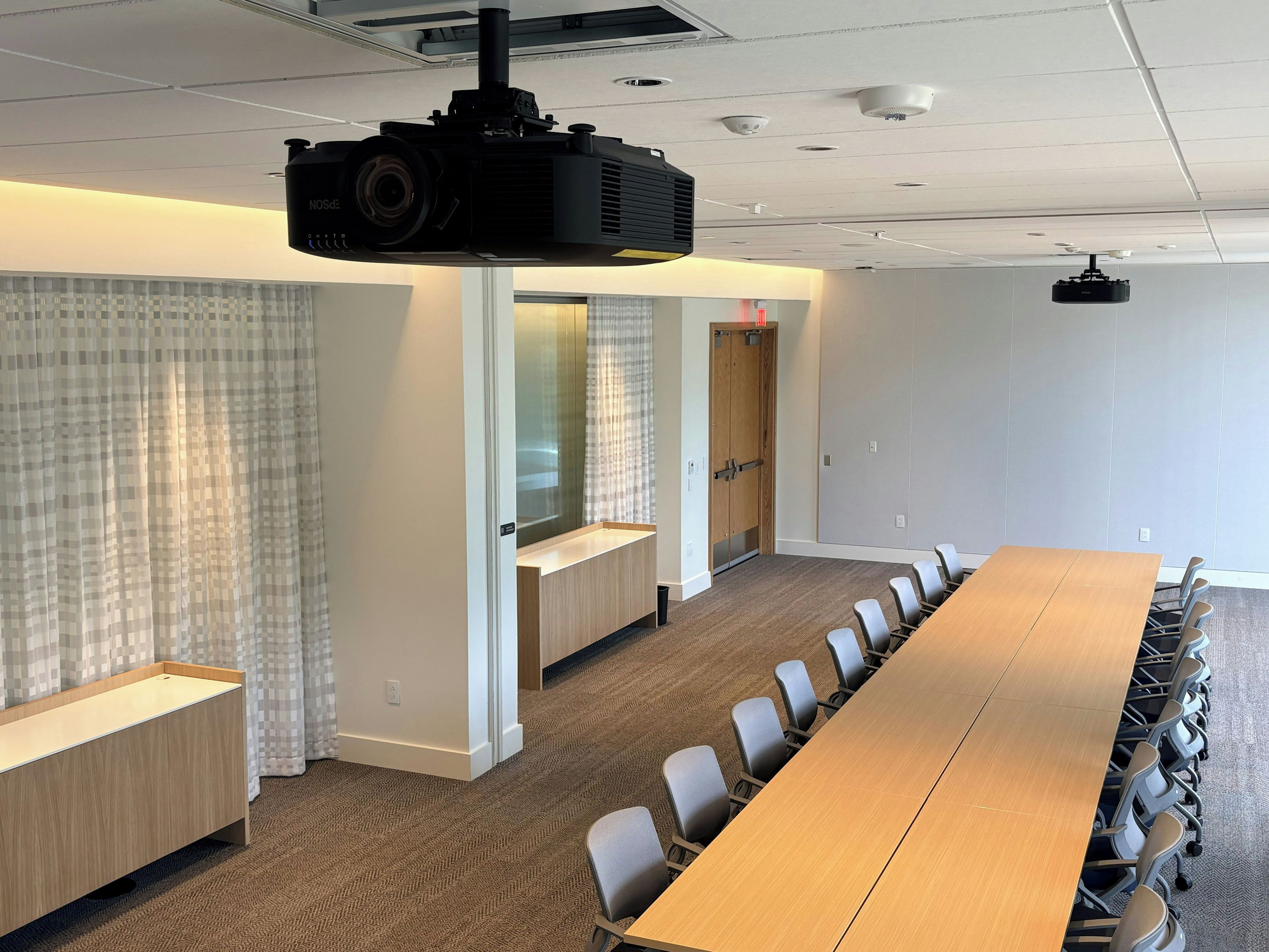 A conference room with a long table, chairs, a projector, and a door.