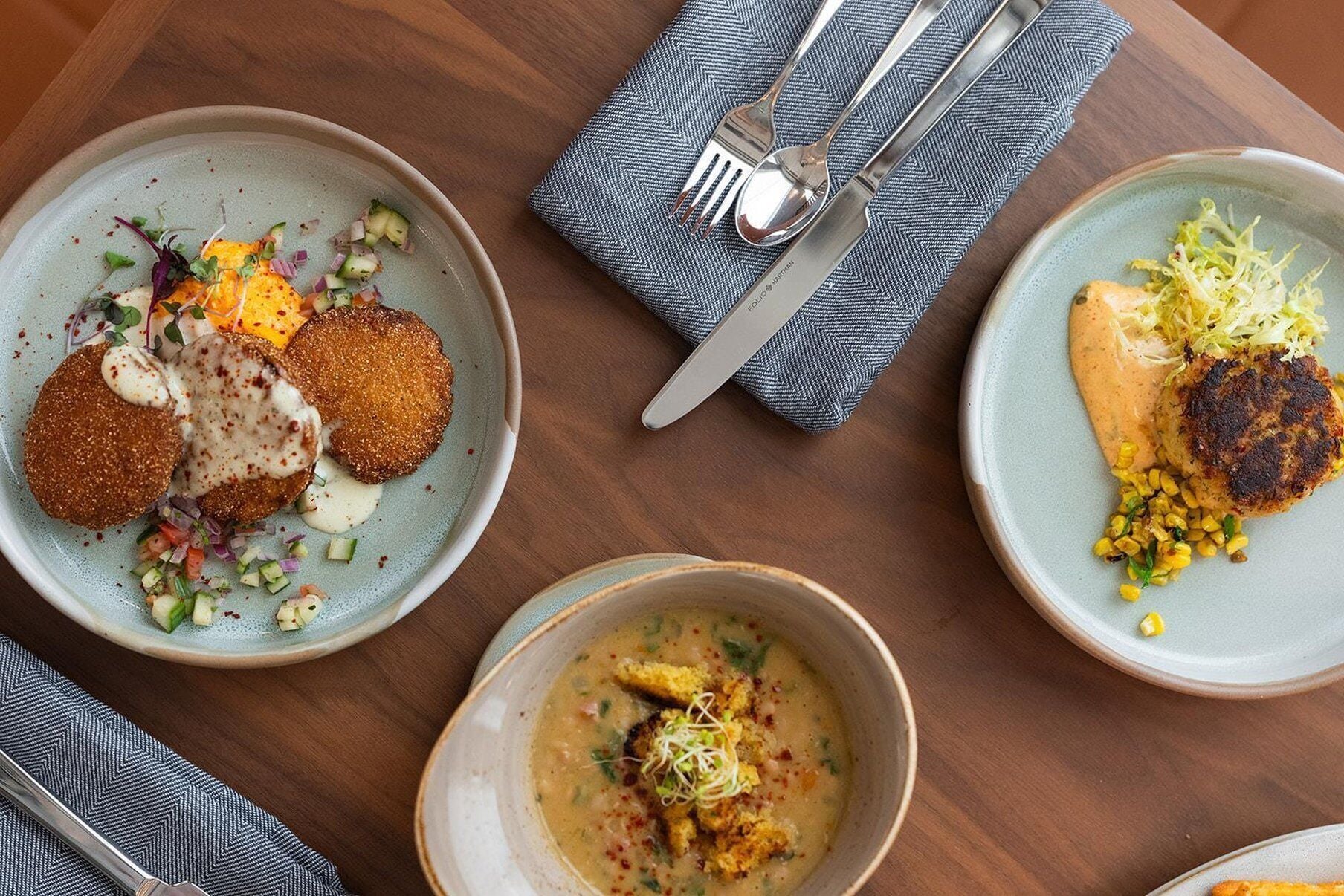 Una mesa con tres platos de comida, cubiertos y una servilleta.