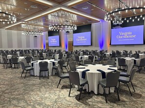 A conference room with multiple tables and chairs, a large screen displaying 'Virginia Guesthouse HOTEL & CONFERENCE CENTER', and a modern ceiling design with lighting fixtures. - Virginia Guesthouse Hotel (Charlottesville)