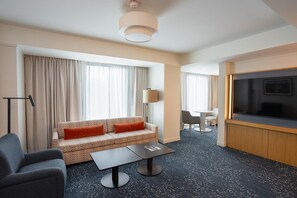 Habitación de hotel con sofá, una pequeña mesa, televisor y zona de comedor.