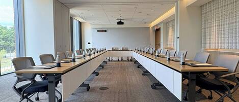 A conference room with a long table, chairs, and a projector screen.
