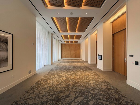 Un pasillo de hotel con alfombra estampada, puertas de madera e iluminación empotrada en el techo.