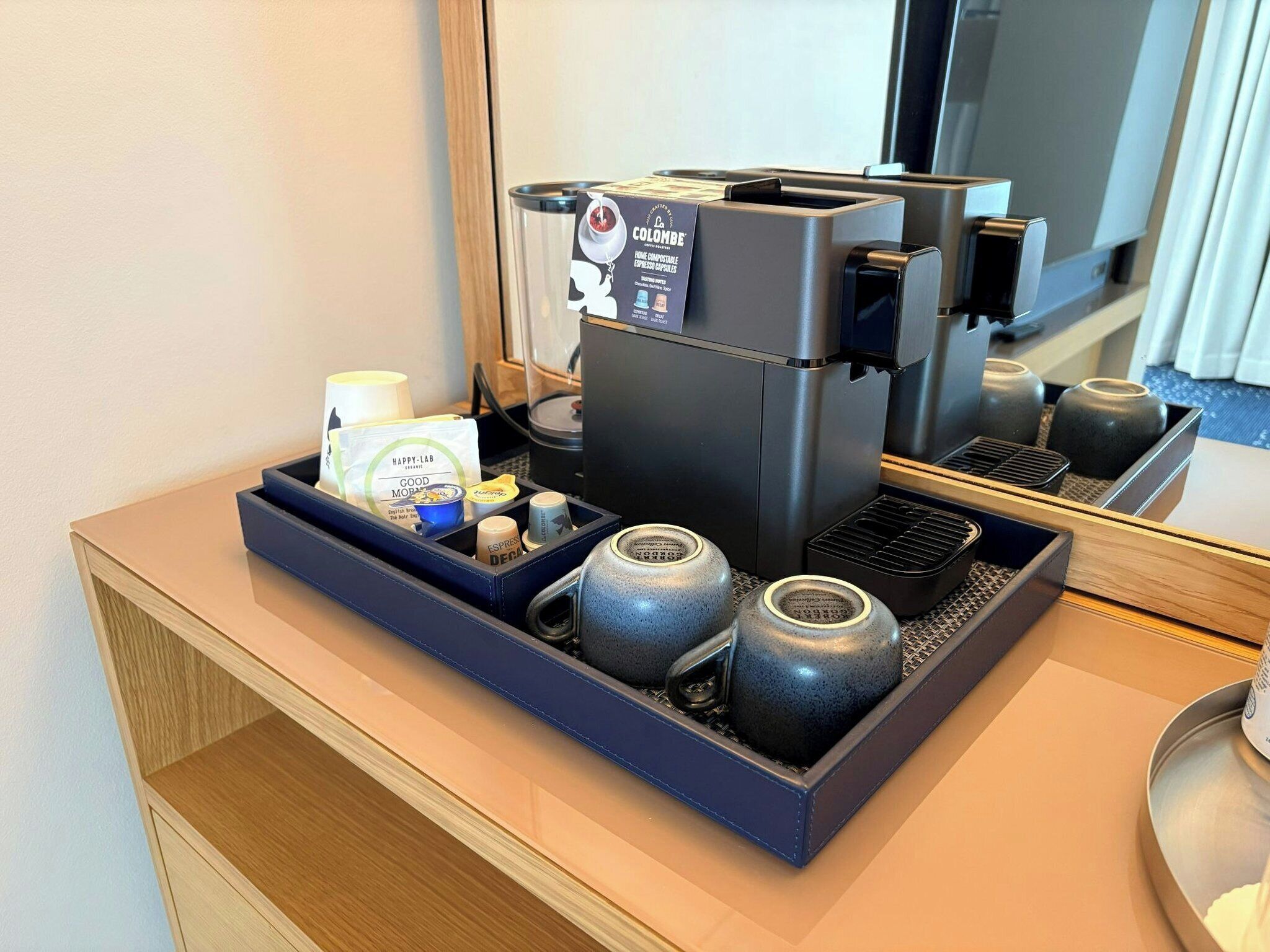 Eine Kaffeemaschine mit Kapselspender, eine Tasse und ein kleiner Becher Sahne auf einer Arbeitsfläche.