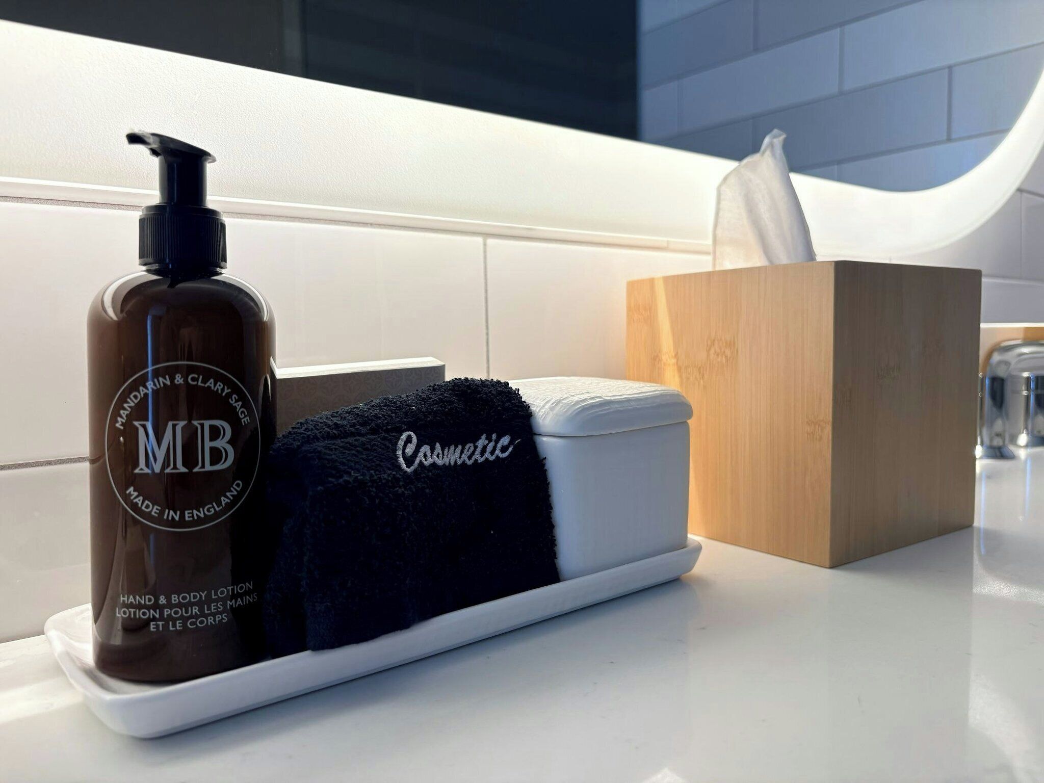 A bathroom counter with a bottle of hand and body lotion, a black towel, a box of tissues, and a small container.