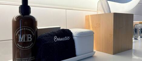 A bathroom counter with a bottle of hand and body lotion, a black towel, a box of tissues, and a small container.