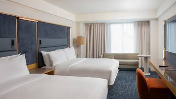 A hotel room with two beds, a desk, a chair, a TV, and a window with curtains.