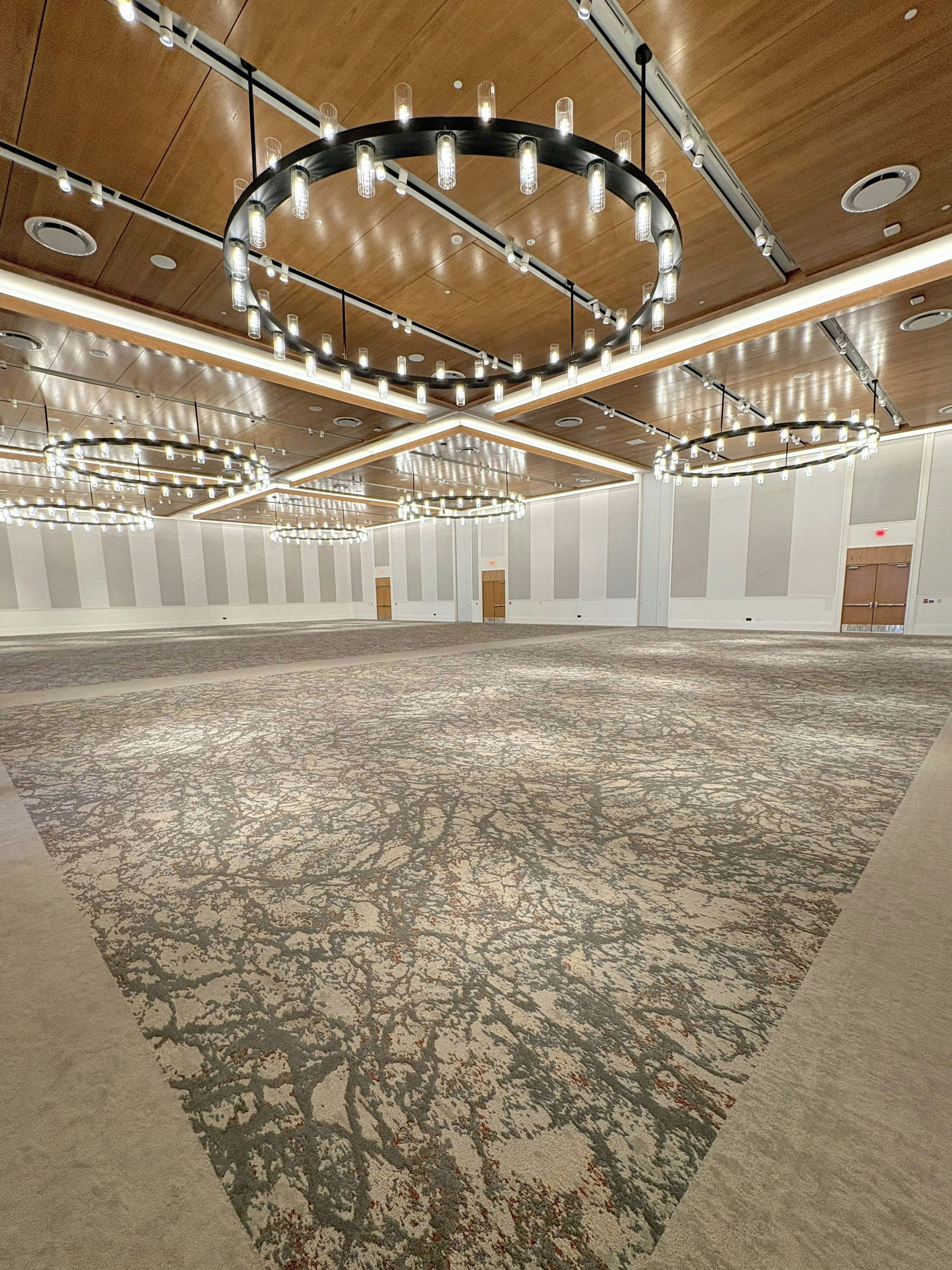 A large, open room with a patterned carpet, multiple chandeliers, and a wooden ceiling.