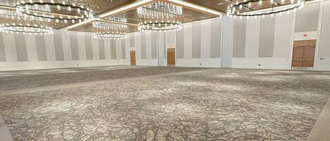 A large, open room with a patterned carpet, multiple chandeliers, and a wooden ceiling.