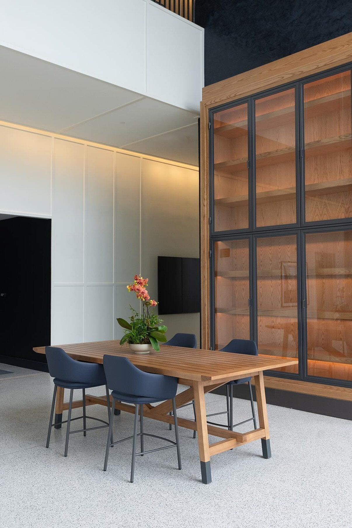 A modern meeting room with a wooden table, four chairs, and a potted plant.
