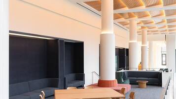 A modern lounge area with a long table, chairs, sofas, and a high ceiling with wooden paneling.