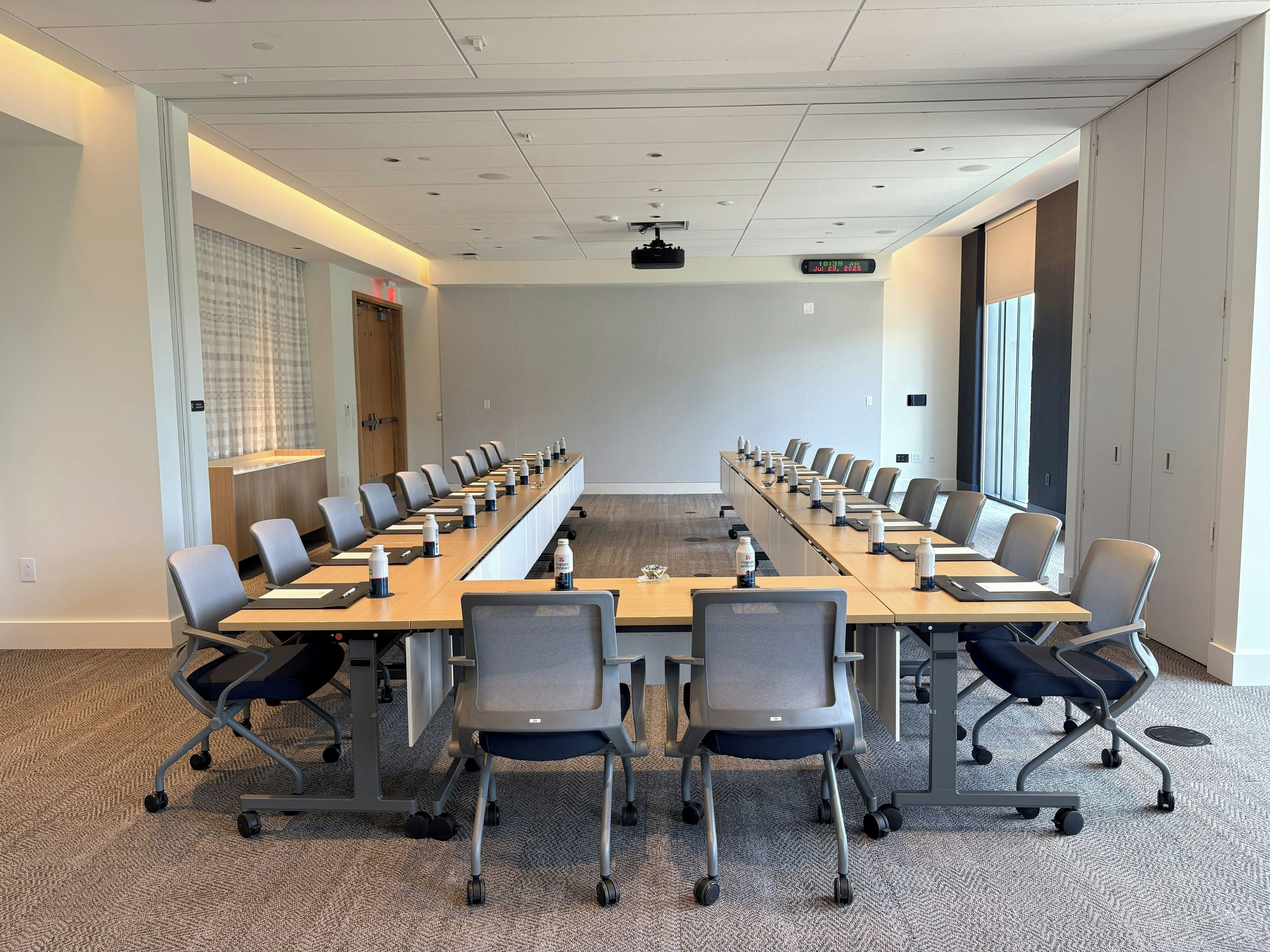 A conference room with a long table, multiple chairs, and a projector screen.