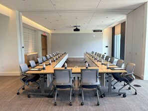 Un salón de conferencias con una larga mesa, varias sillas y una pantalla para proyector.