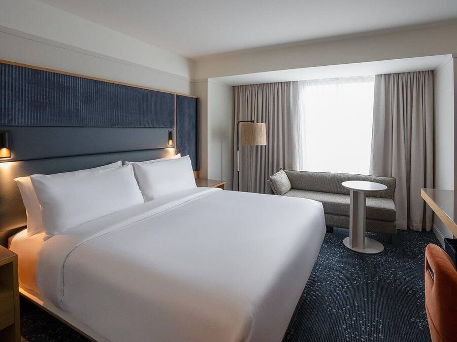 A hotel room with a large bed, a sofa, a small round table, and a TV.