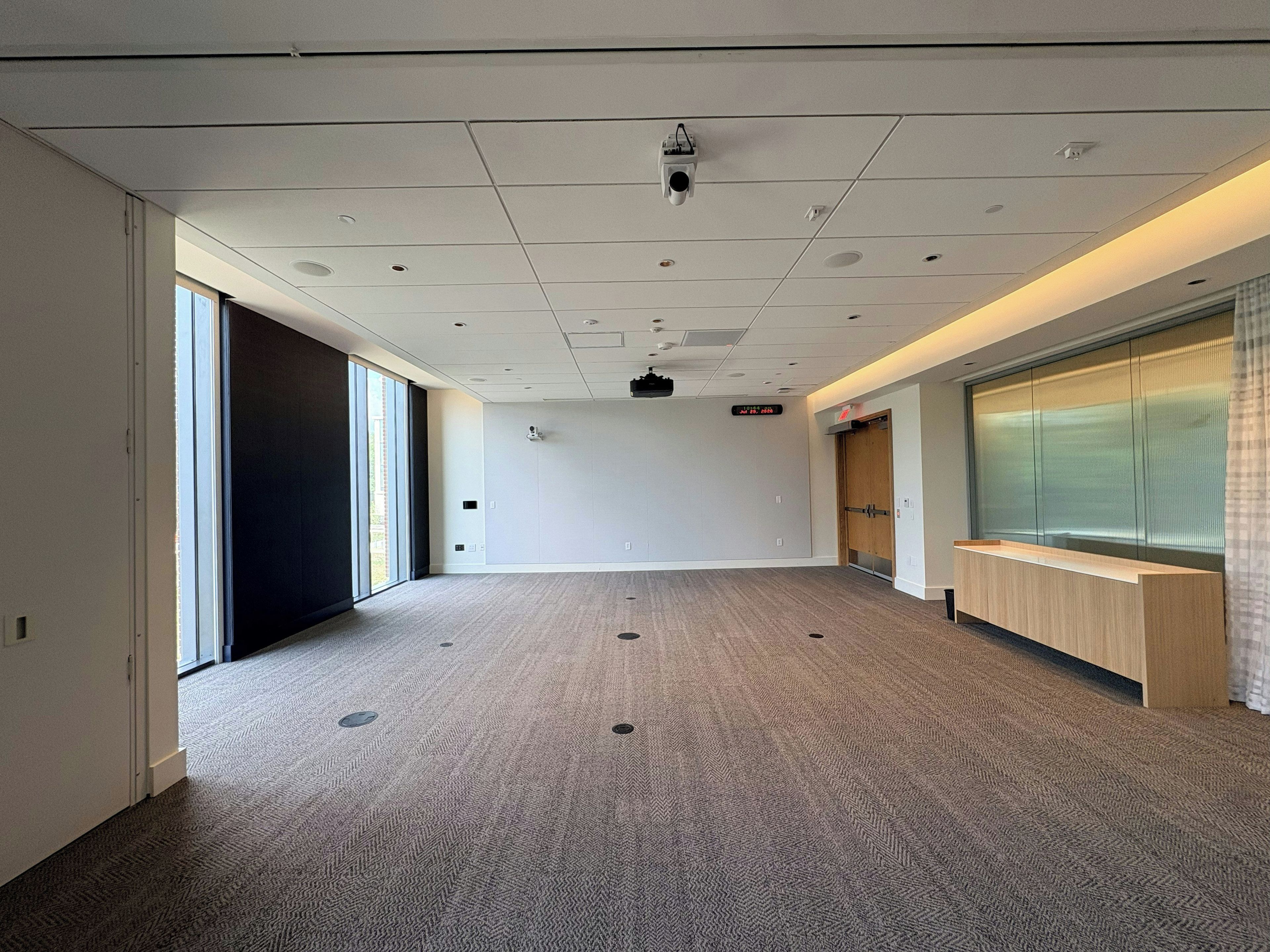A conference room with a carpeted floor, a projector, a digital clock, and a reception desk.