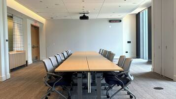 A conference room with a long table, chairs, carpeted floor, ceiling lights, and a projector.
