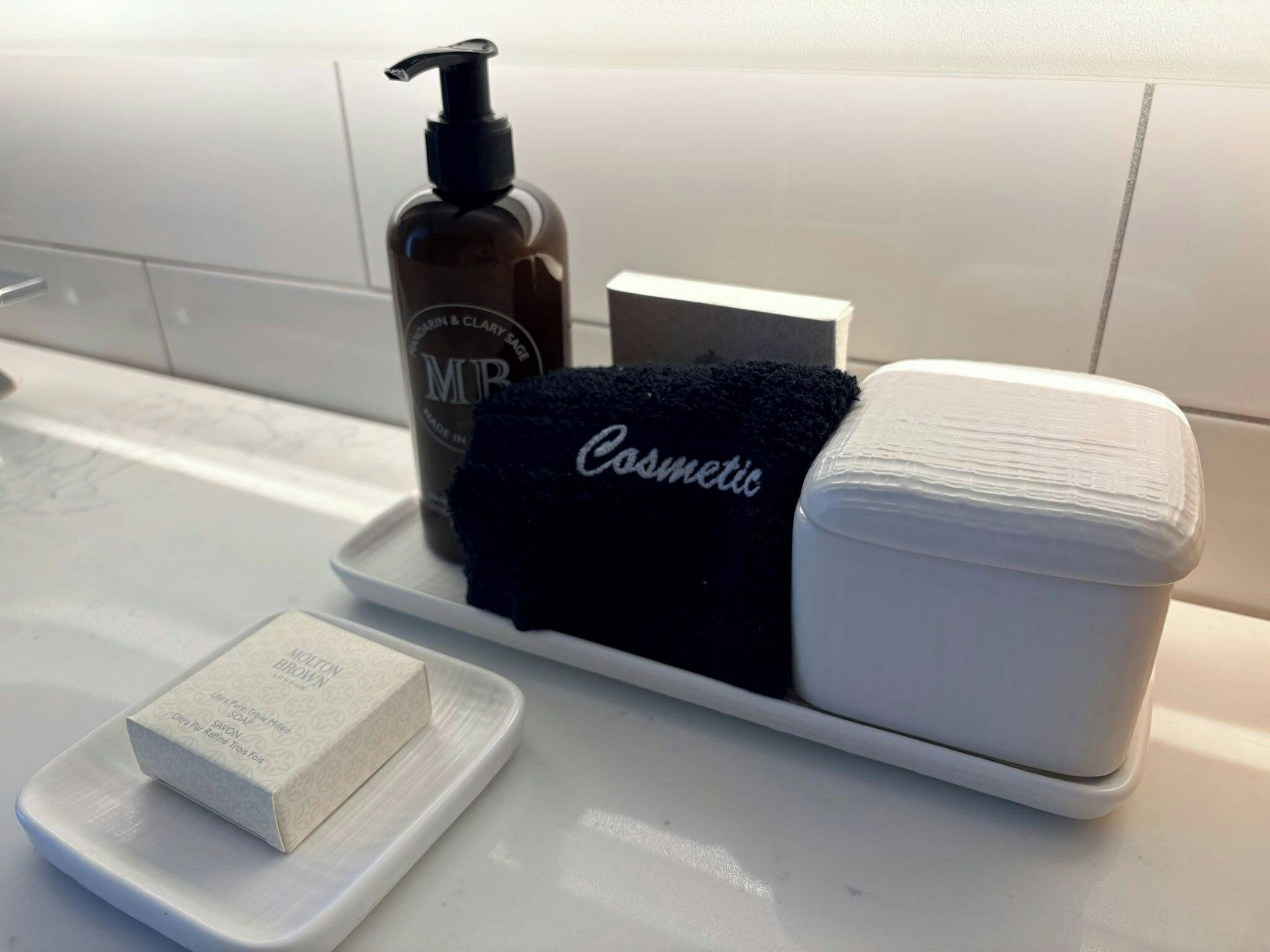 Ein Badezimmer-Waschtisch mit Pflegeartikeln, darunter eine Seife, eine Shampooflasche, ein schwarzes Handtuch und eine Lotioncreme.