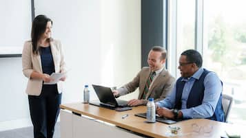 A business meeting in a modern office with a large window, a wooden desk, and a laptop.