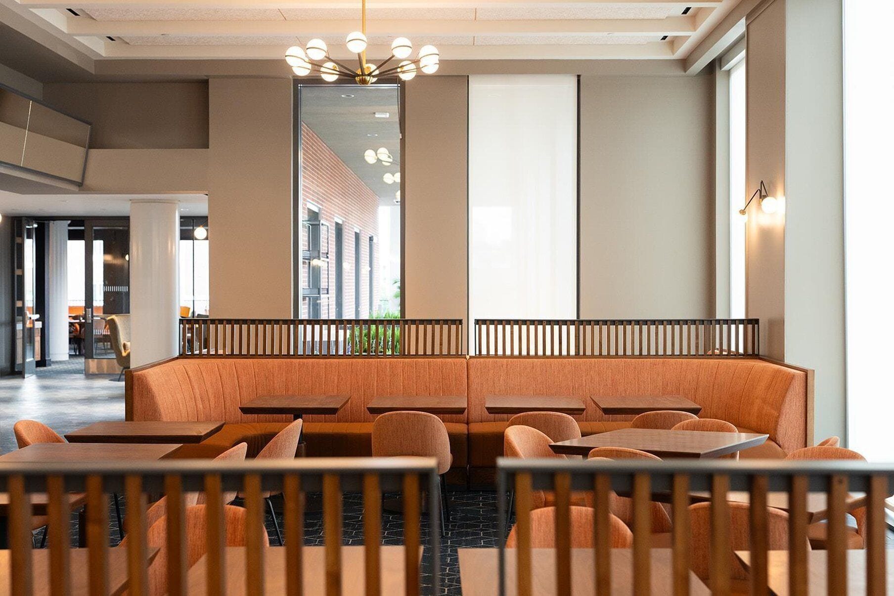 Un interior de restaurante moderno con una zona de asientos central, mesas individuales y un gran ventanal con vistas al exterior.