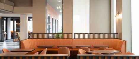 Un interior de restaurante moderno con una zona de asientos central, mesas individuales y un gran ventanal con vistas al exterior.