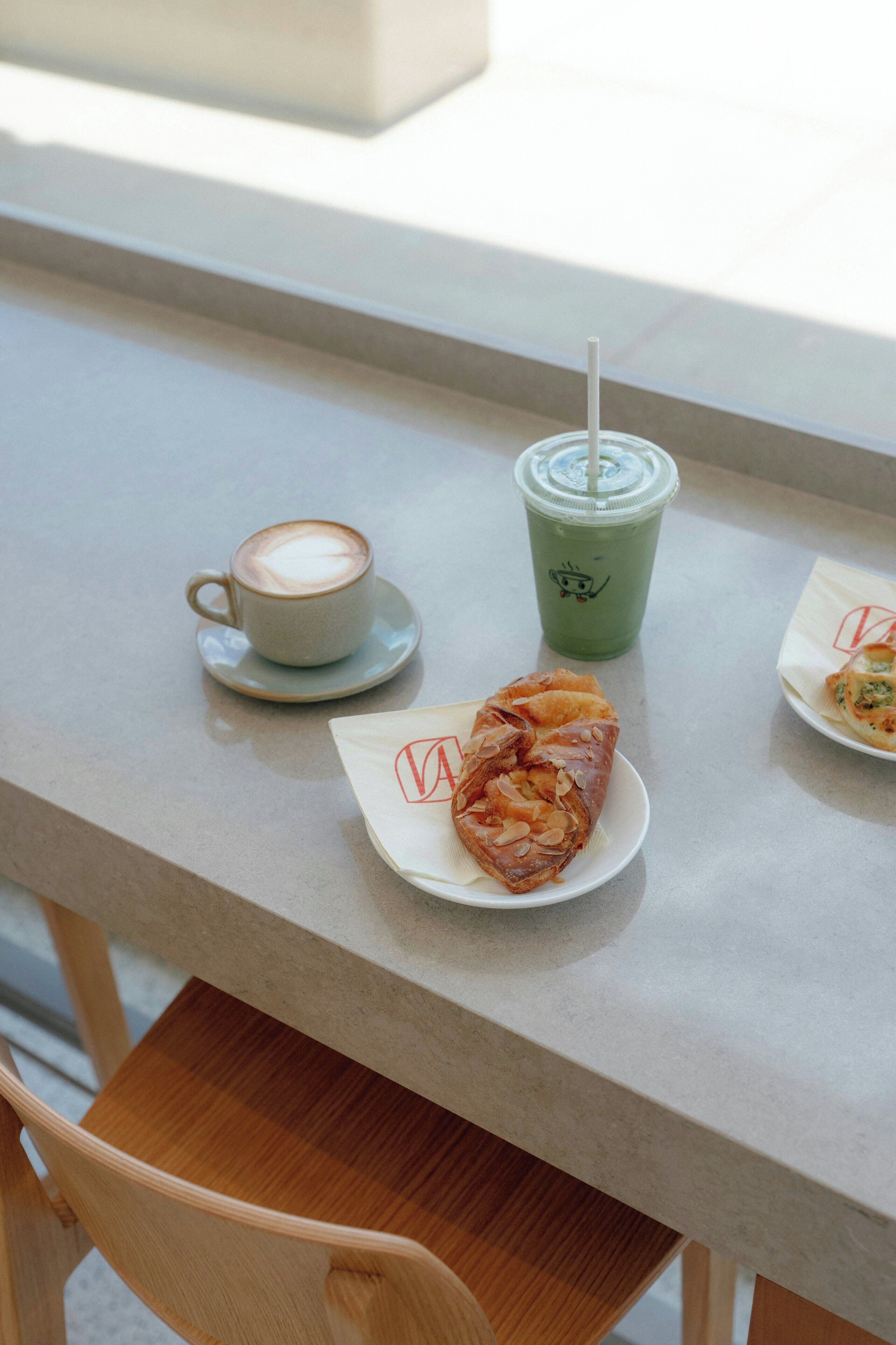 A table with a cup of coffee, a green drink with a straw, and a pastry on a plate.